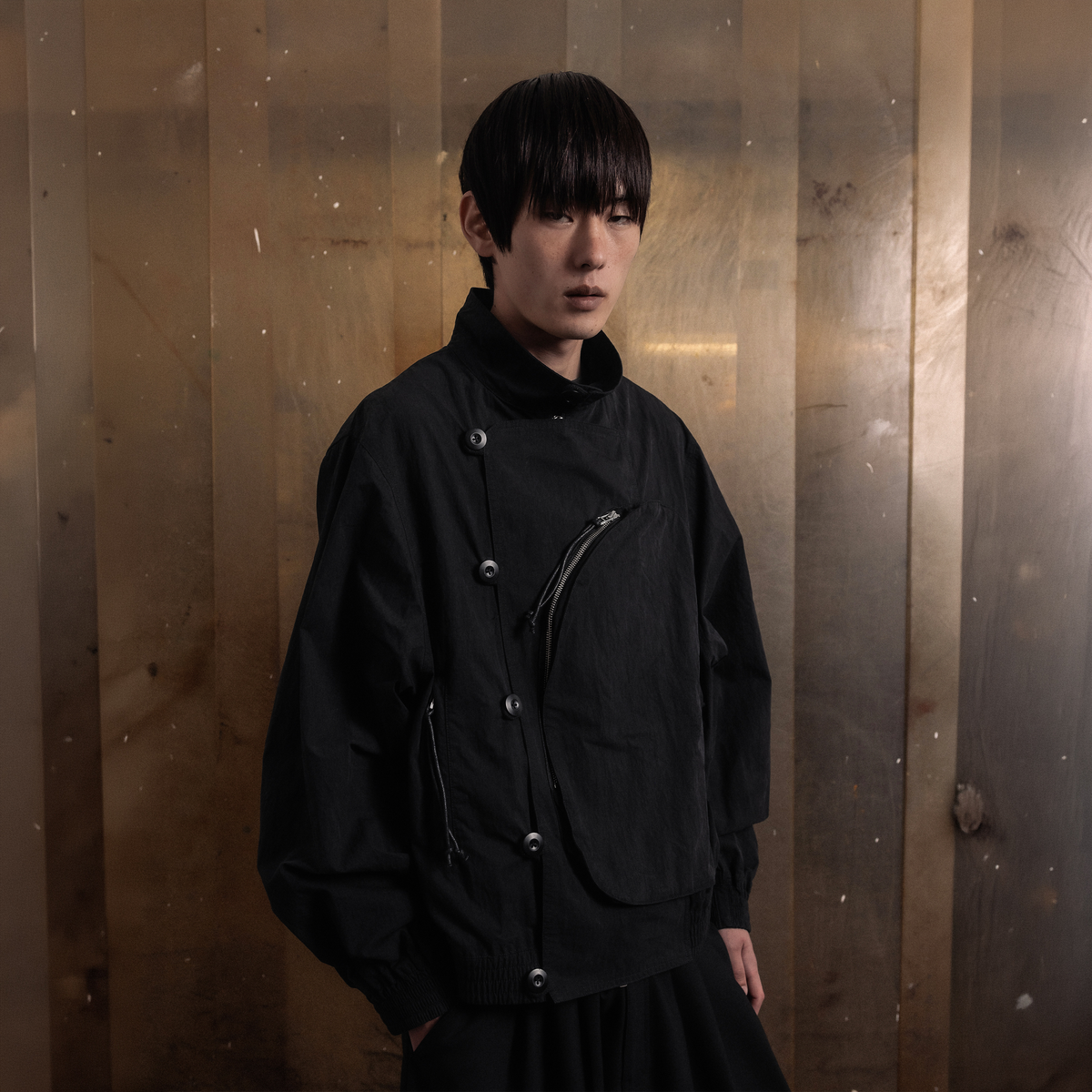 SCRT Distorted Blouson Jacke in Schwarz, Model leicht gedreht vor Metallwand